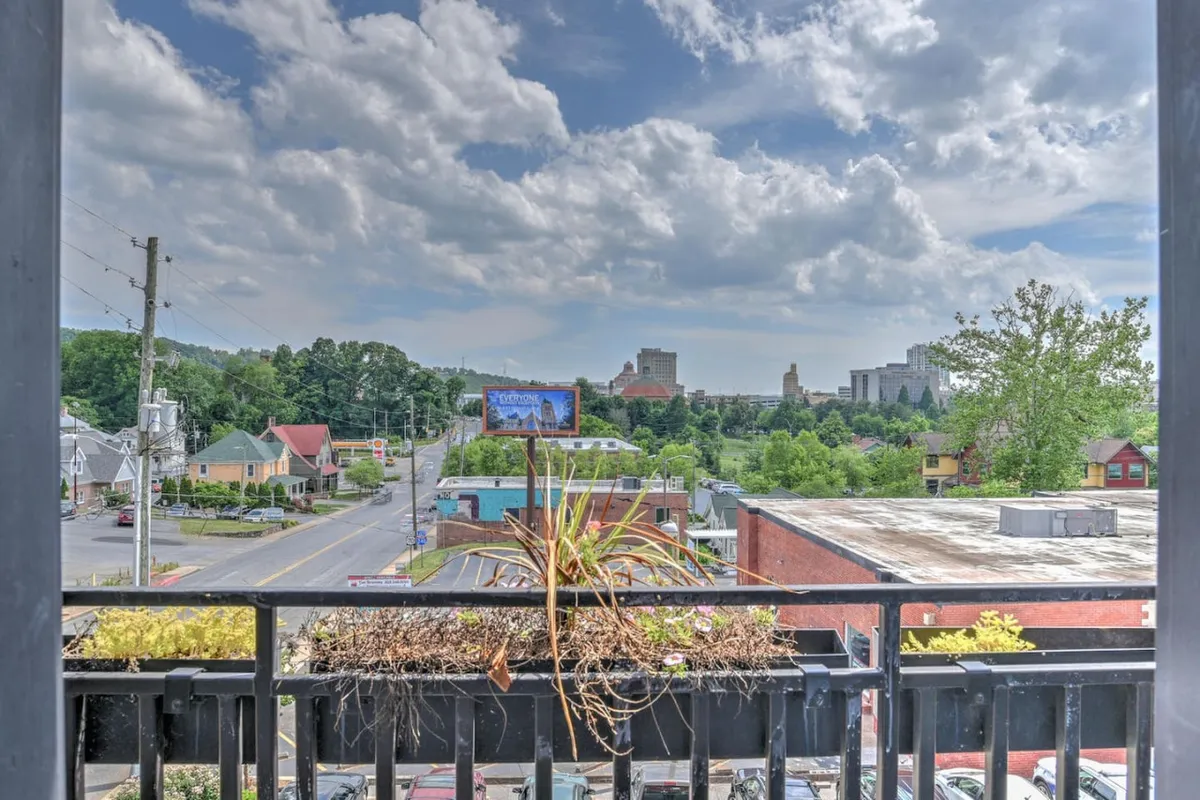 A serene balcony view overlooking Asheville’s city skyline and distant mountains, framed by a balcony railing. The image invites viewers to imagine relaxing outdoors while soaking in the sunset or cityscape, connecting the condo to the broader city environment.