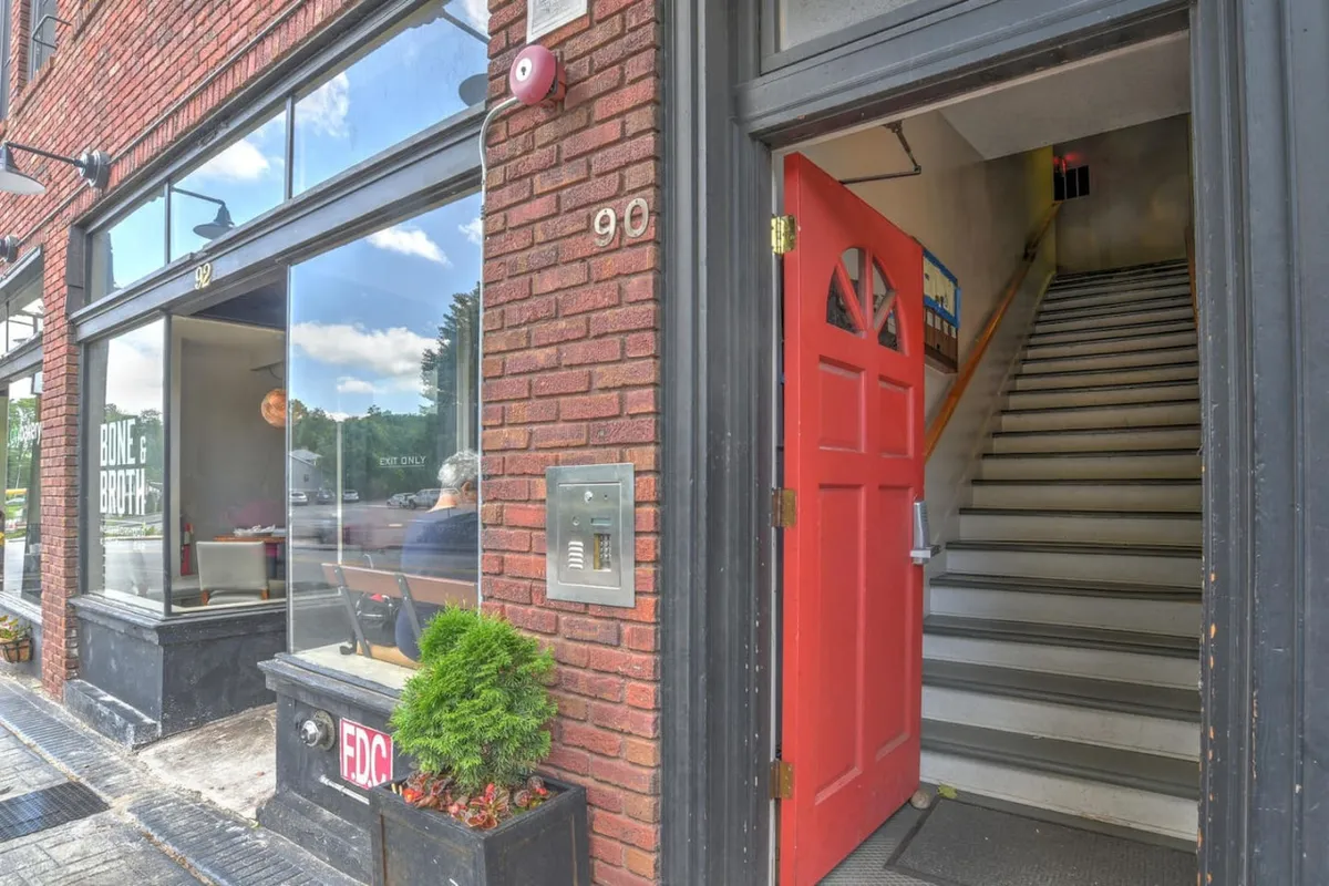 The image highlights a welcoming restaurant entrance with a distinctive red door set in a brick facade and large windows. Diners and passersby are visible, evoking the sense of a dynamic neighborhood where food and socializing are central to daily life.