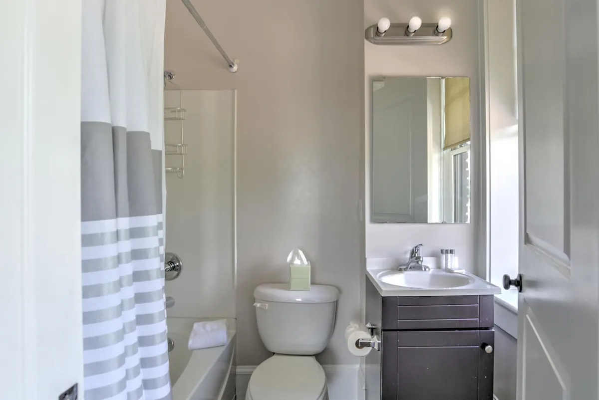 A modern bathroom featuring a bathtub, toilet, sink, large mirror, and a window for natural light. The space feels refreshing and calm, perfect for unwinding after a busy day exploring the city.