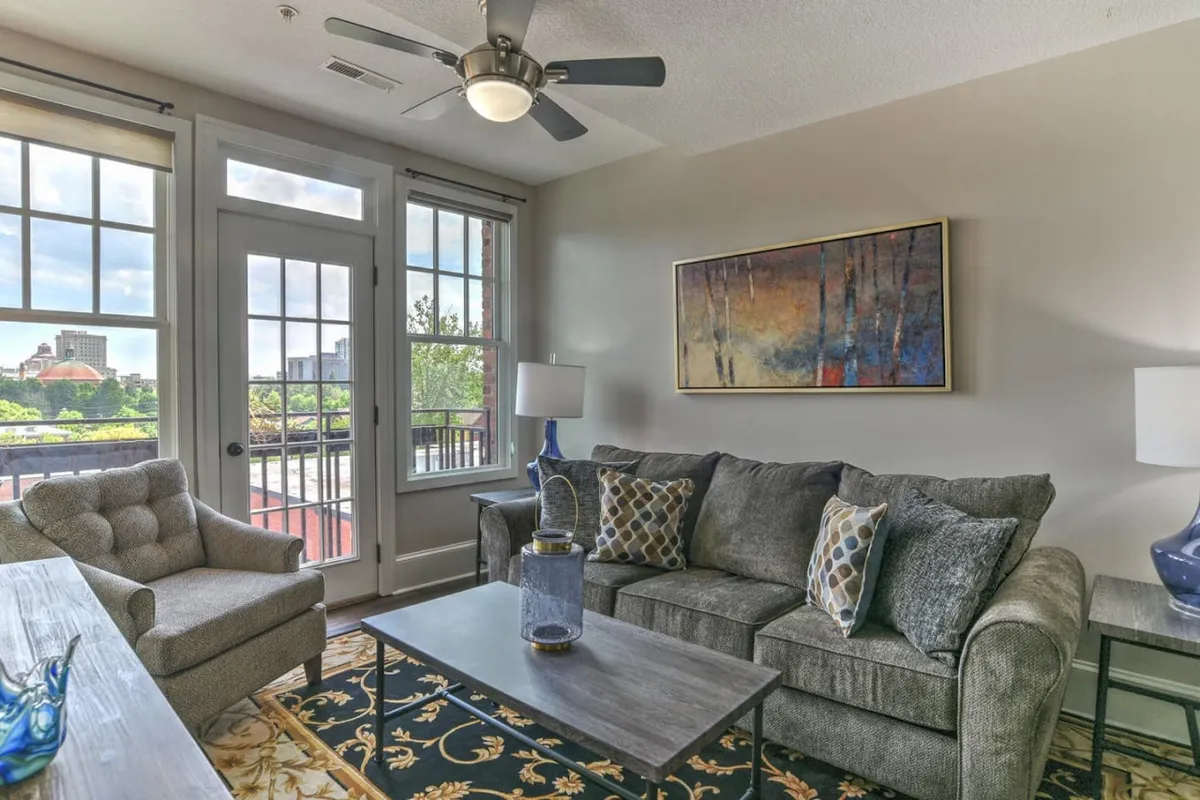 A comfortable sitting area with a sofa, coffee table, interesting artwork, and bright windows bringing in city light. The space feels both timeless and updated, encouraging relaxation upon arrival.