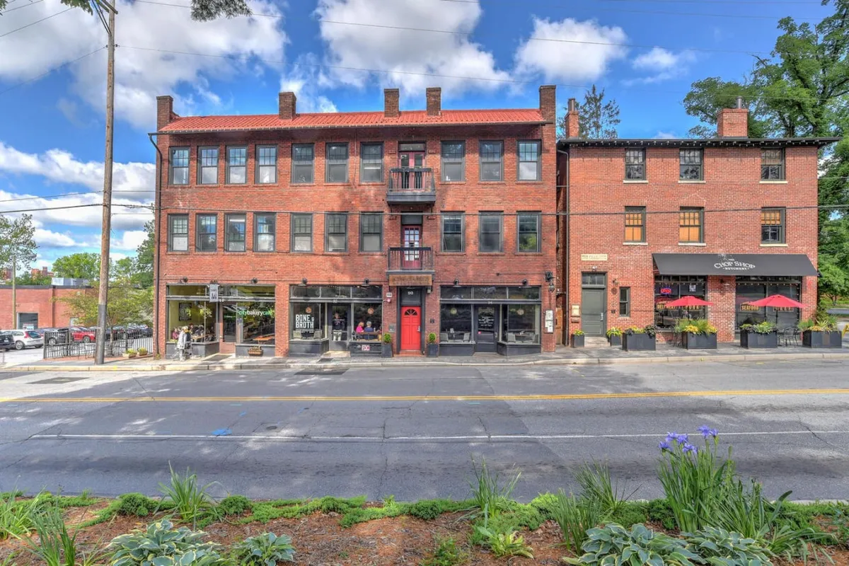 This exterior shot captures a welcoming red door, accessible balcony, and nearby storefronts along a vibrant street. The image conveys easy access to neighborhood amenities such as coffee shops and bistros, while hinting at the lively, walkable environment just outside the residence.