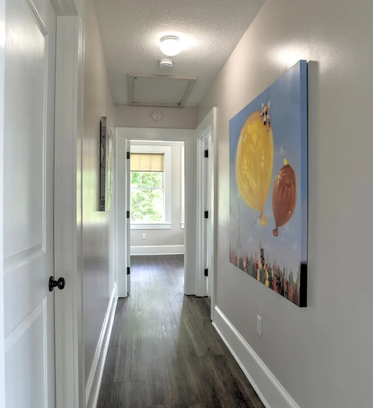 A sunlit hallway featuring dark wood flooring, vibrant balloon-themed artwork on the wall, and natural light streaming in from a nearby window. The space feels open and inviting, emphasizing a blend of artistic flair and the building's historic character.