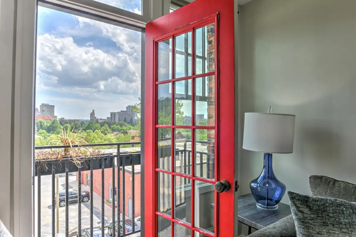 A view of the red glass door flanked by a blue lamp and a cozy sofa, with natural light filtering in. The scene radiates warmth and character, with the red door acting as an eye-catching historic feature, complemented by stylish modern furnishings.