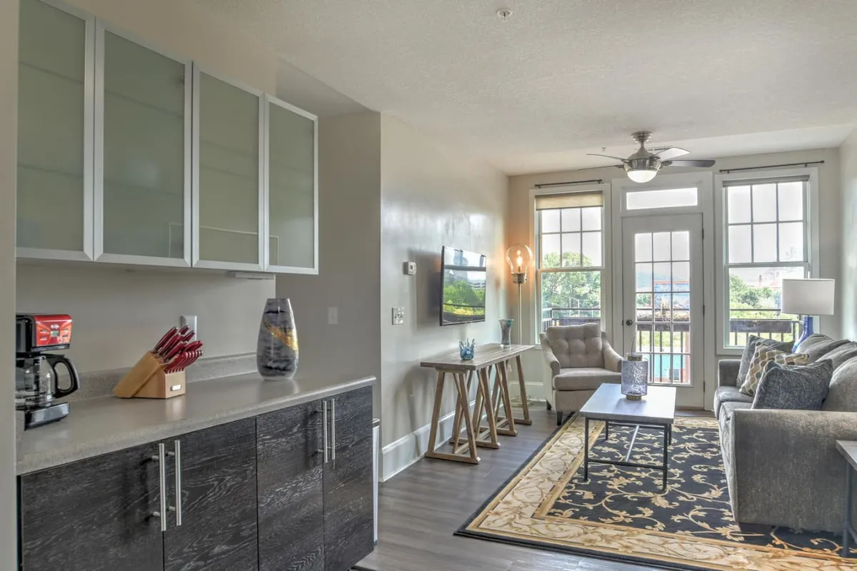 The hero image showcases a stylish, sunlit living room with a plush sofa, a modern coffee table, tasteful wall art, and large windows that bathe the space in natural light. The inviting setup hints at cozy mornings with coffee or relaxed evenings shared with friends, while the historic architectural details add character and charm.