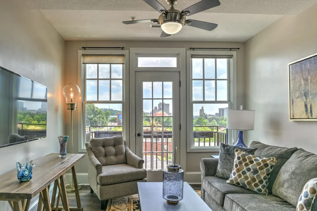 A cozy living room with a sofa and armchair, coffee table, and large windows that reveal a view outside. The space is set up for relaxation, entertaining guests, and enjoying the scenery through the windows, suggesting a connection to the vibrant city just beyond.