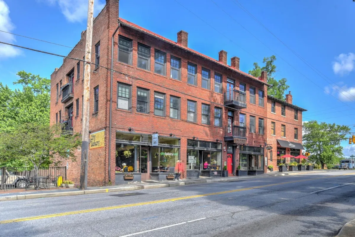 This image captures the lively red brick facade of the King James Building, featuring large windows, a balcony, and active storefronts at street level. It showcases people enjoying the vibrant sidewalk, hinting at nearby boutiques, coffee shops, and a thriving local culture.